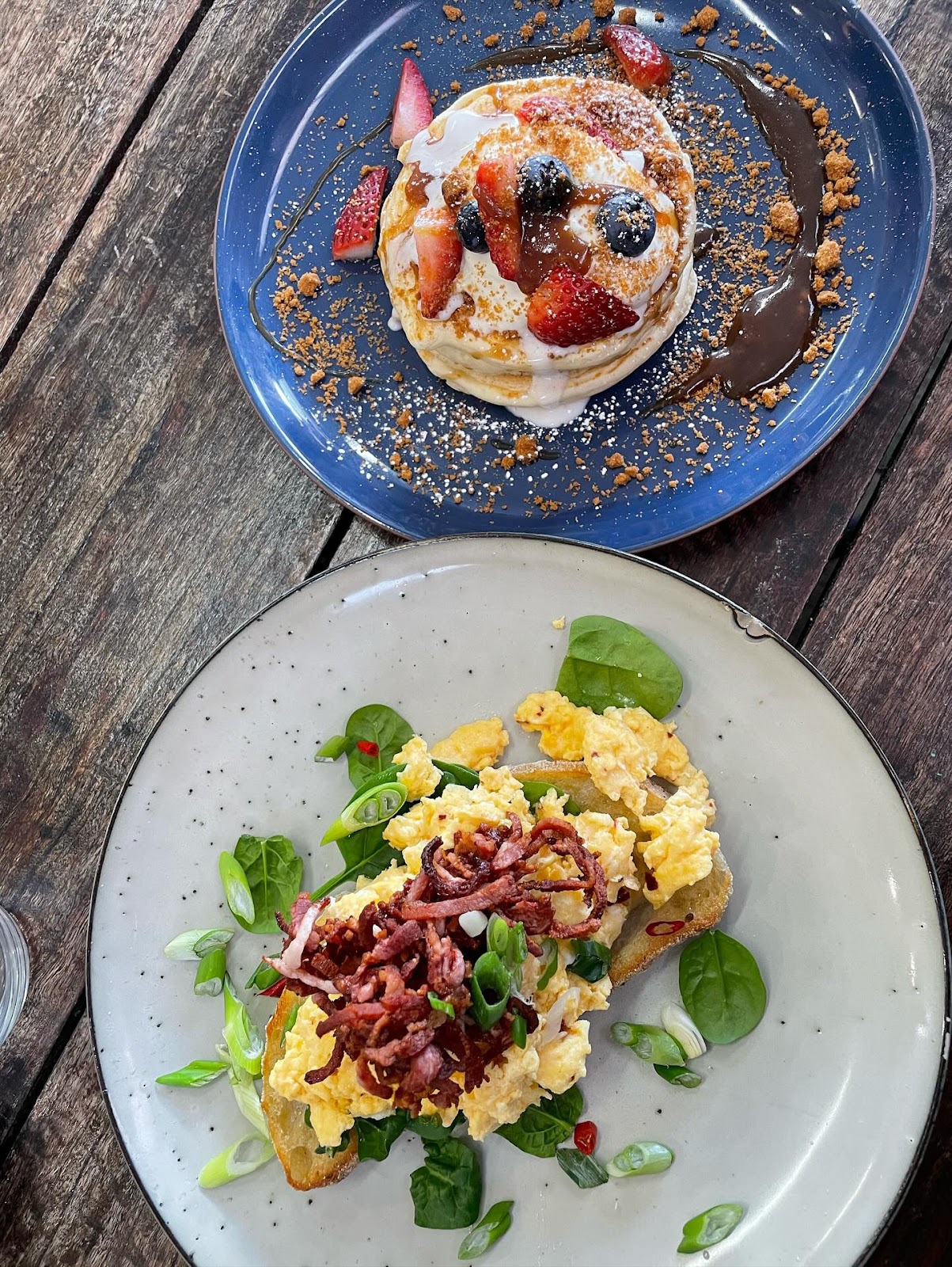Pancakes with berries beside scrambled eggs and bacon on toast